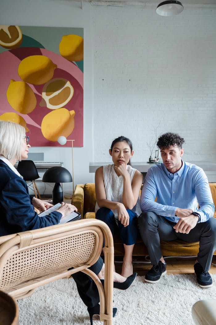 A couple sits on a sofa in therapy session with a counselor, discussing relationship issues.
